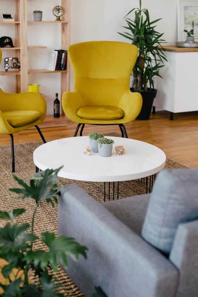 A relaxed office lounge area with mustard-yellow chairs, a round coffee table, and greenery.