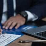 Business professional reviewing documents at desk with laptop.
