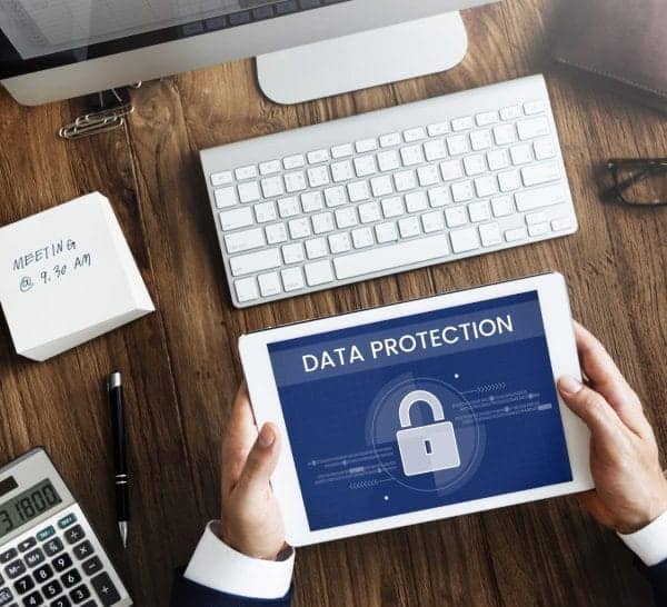 Person holding tablet with data protection lock icon, office desk setup.