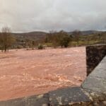 Raging river floodwaters during a windy weekend in a rural landscape.
