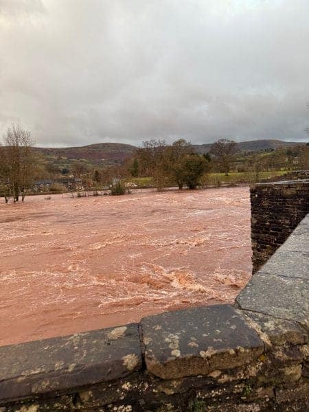 Raging river floodwaters during a windy weekend in a rural landscape.