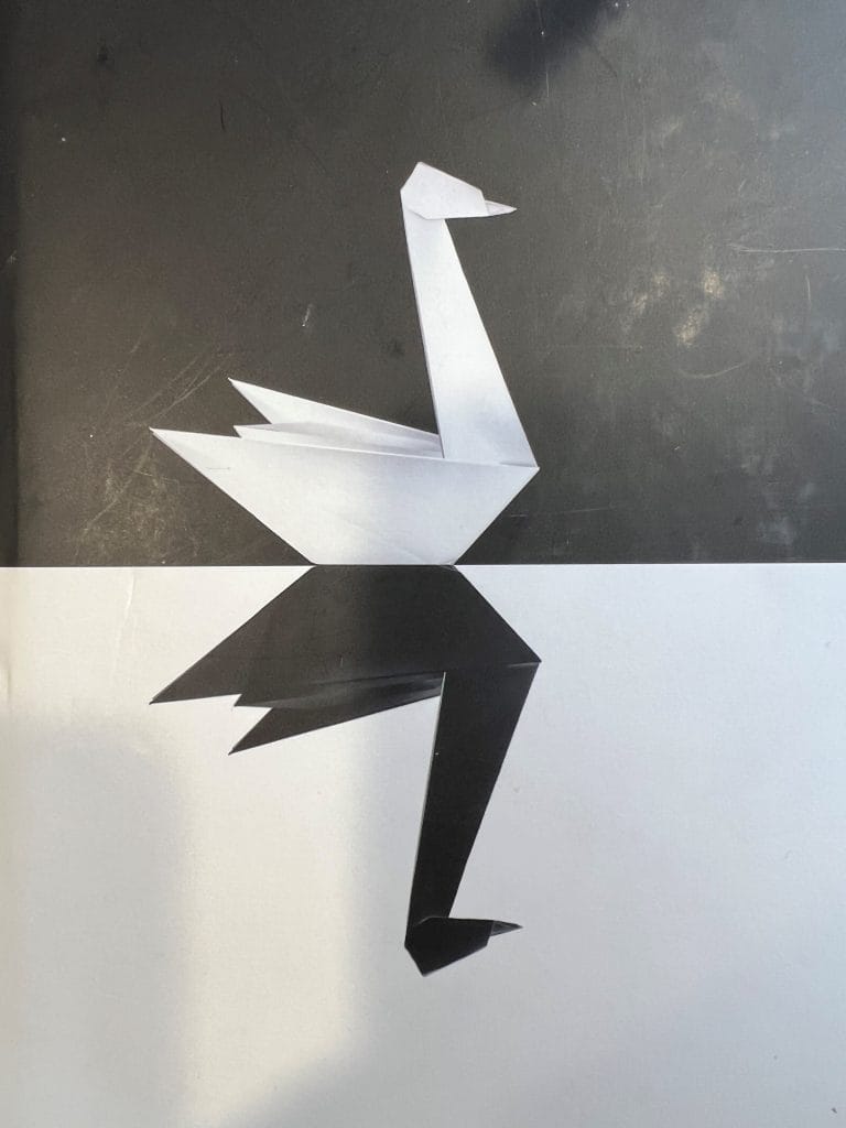 Origami paper swan with reflection on black and white surface.