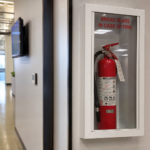 Fire extinguisher behind break glass panel in an office corridor — the emergency plan nobody reaches for