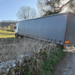 Articulated lorry stuck on a dry stone wall after taking the restricted-weight and height access road.