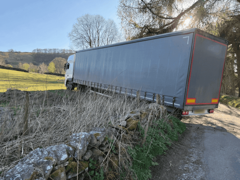 Articulated lorry stuck on a dry stone wall after taking the restricted-weight and height access road.