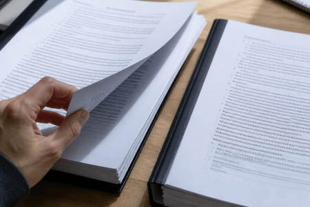 Hand comparing two printed policy documents side by side in binders