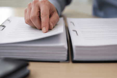 Hand flipping through pages in a thick ring binder next to a second binder