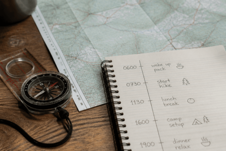 Hand-drawn hiking itinerary timetable next to a map and compass