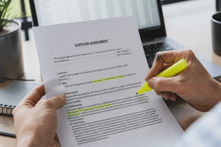 Person highlighting key clauses on a printed supplier agreement contract