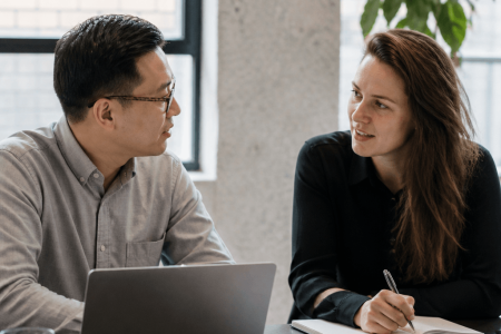 Consultant and client in conversation, one taking notes while the other uses a laptop