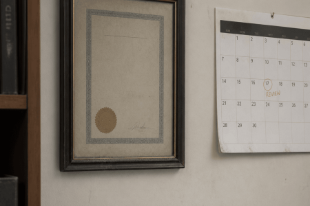 Framed certification hanging on an office wall beside a wall calendar marked for review