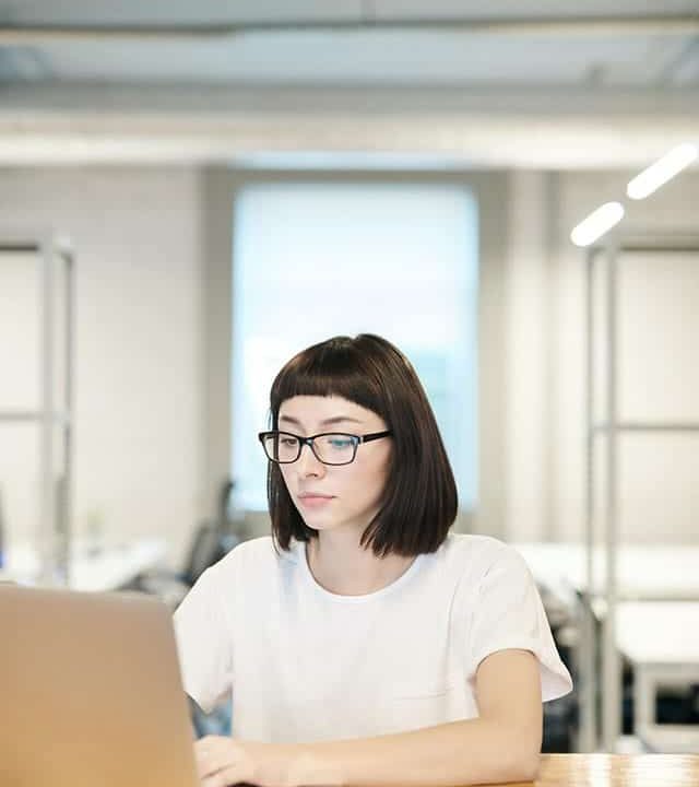 Woman working on a laptop at a wooden desk in a modern office